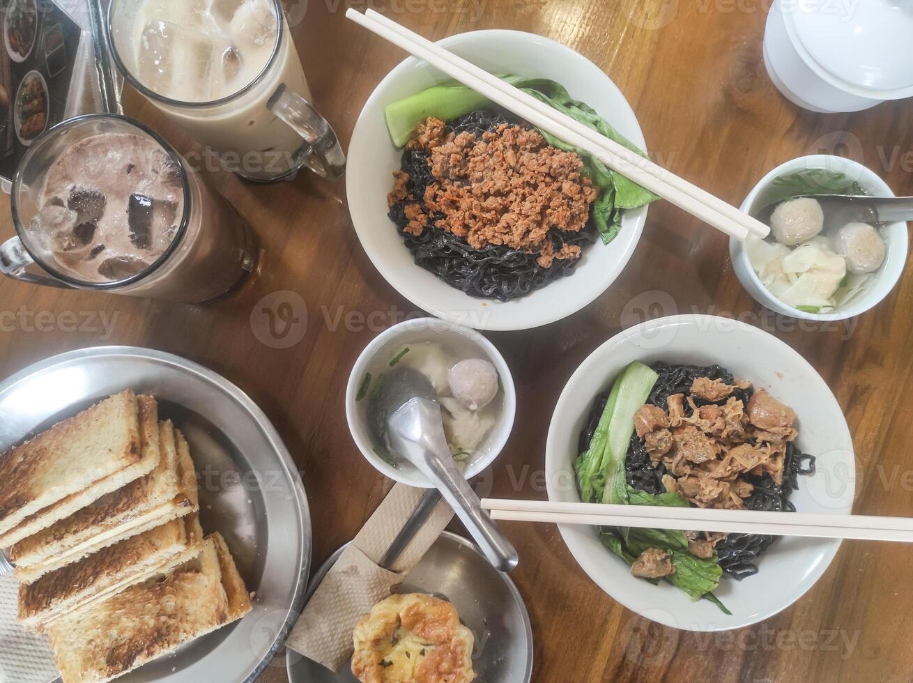 Tabletop shot of a typical Indonesian lunch menu. The dish consists of chicken noodles with meatball soup, a cold chocolate drink, and desserts of toast and egg tart. Indonesian gourmet variation. photo