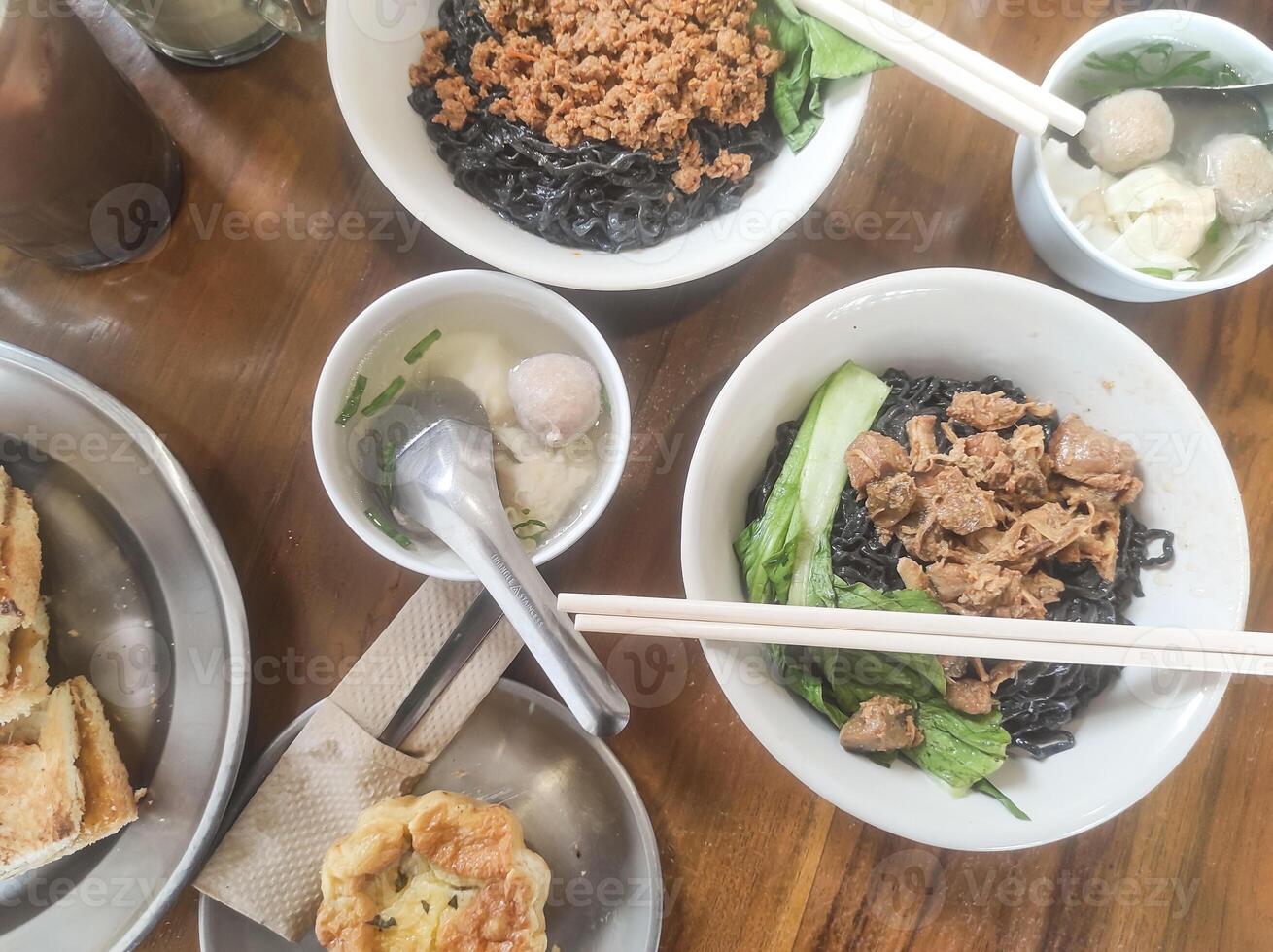 Tabletop shot of a typical Indonesian lunch menu. The dish consists of chicken noodles with meatball soup, a cold chocolate drink, and desserts of toast and egg tart. Indonesian gourmet variation. Ads photo
