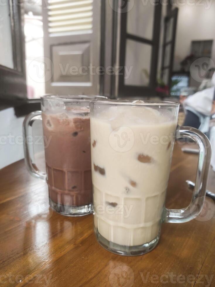 Tabletop shot A pair of cold drinks. A cold chocolate drink next to a cold vanilla drink served with a large glass held on a brown wooden table. Tasty Beverage with copy space photo