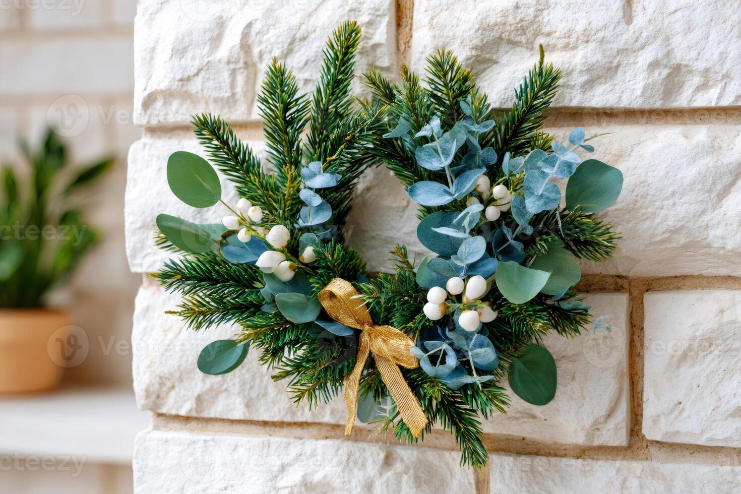 Christmas wreath with eucalyptus, white berries and golden ribbon hanging on a white brick wall photo