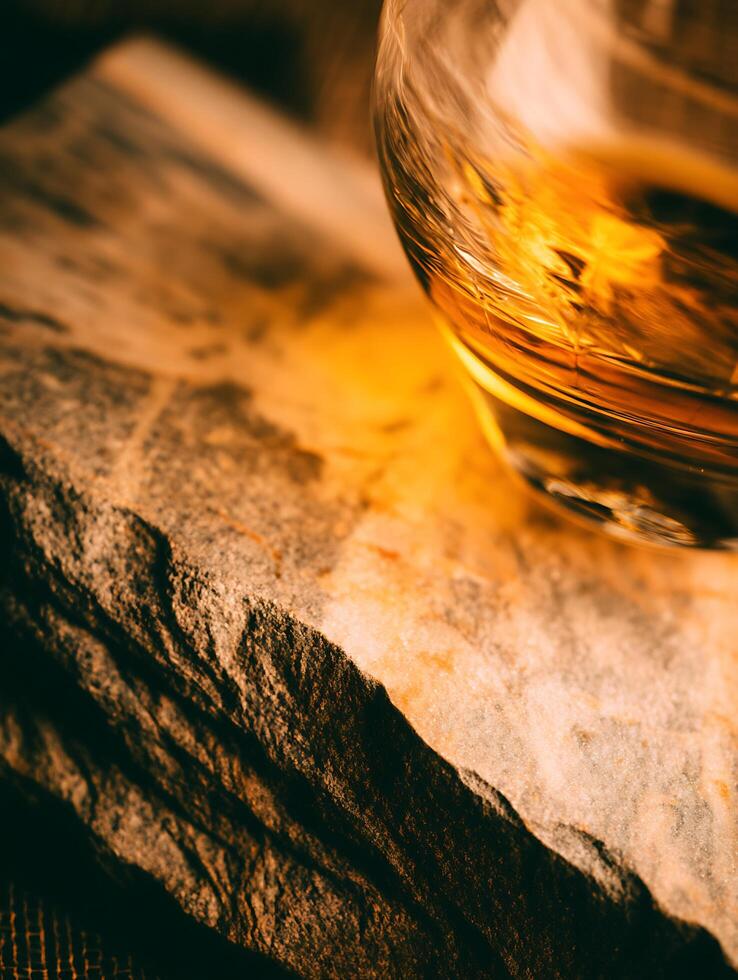 Amber Liquid in Glass on Rough Stone Surface. Close up of a golden beverage resting on textured rocks. photo