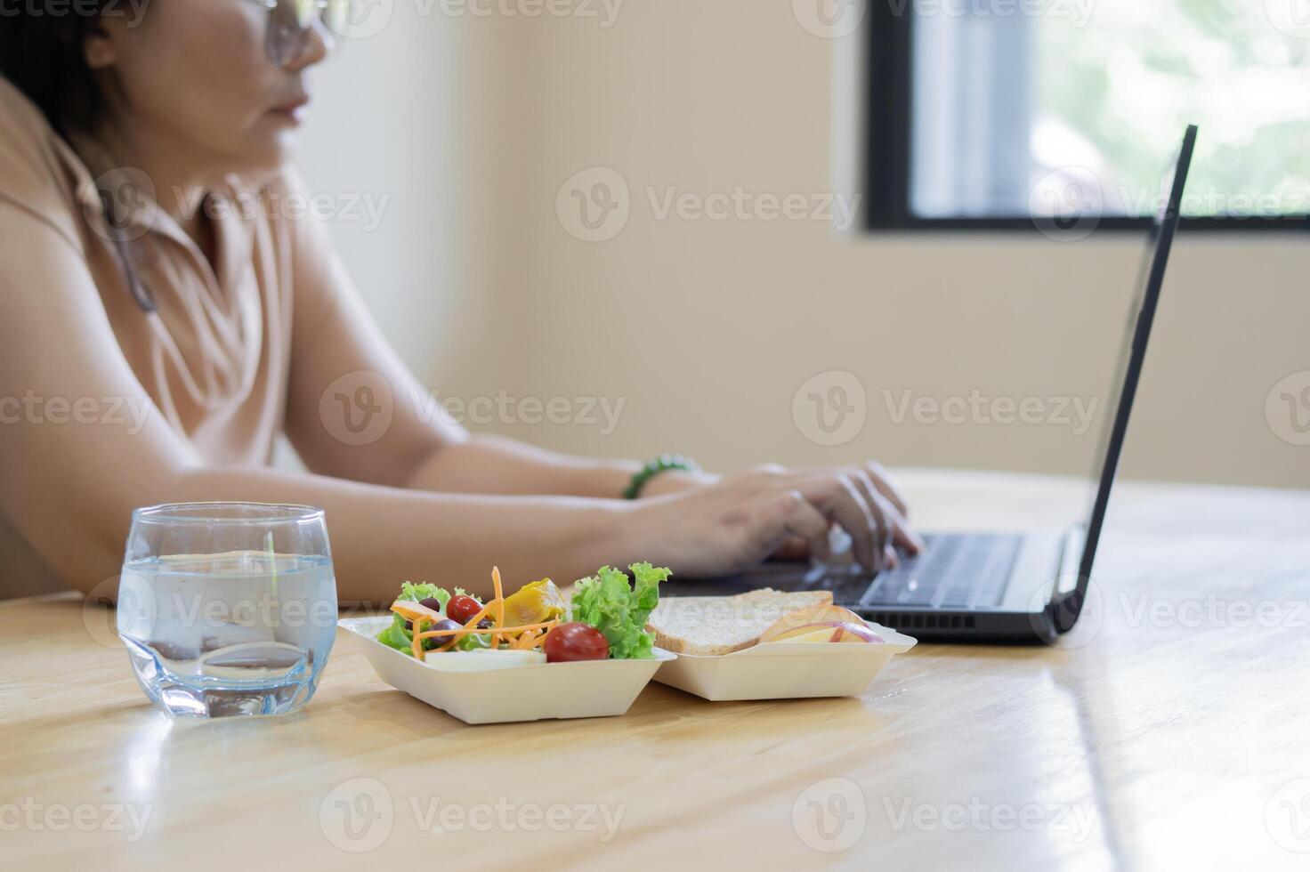 Woman office worker sitting at desk with laptop and glass of water with healthy boxed food photo