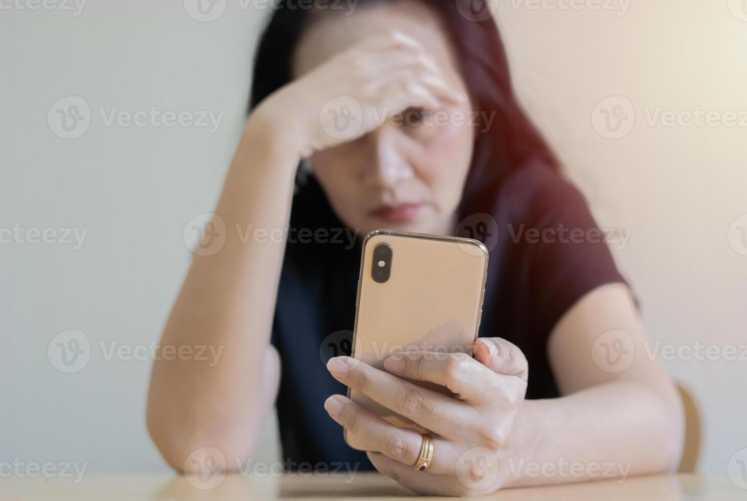 Sad woman sitting at the table with smartphone and worried with problem at home. photo
