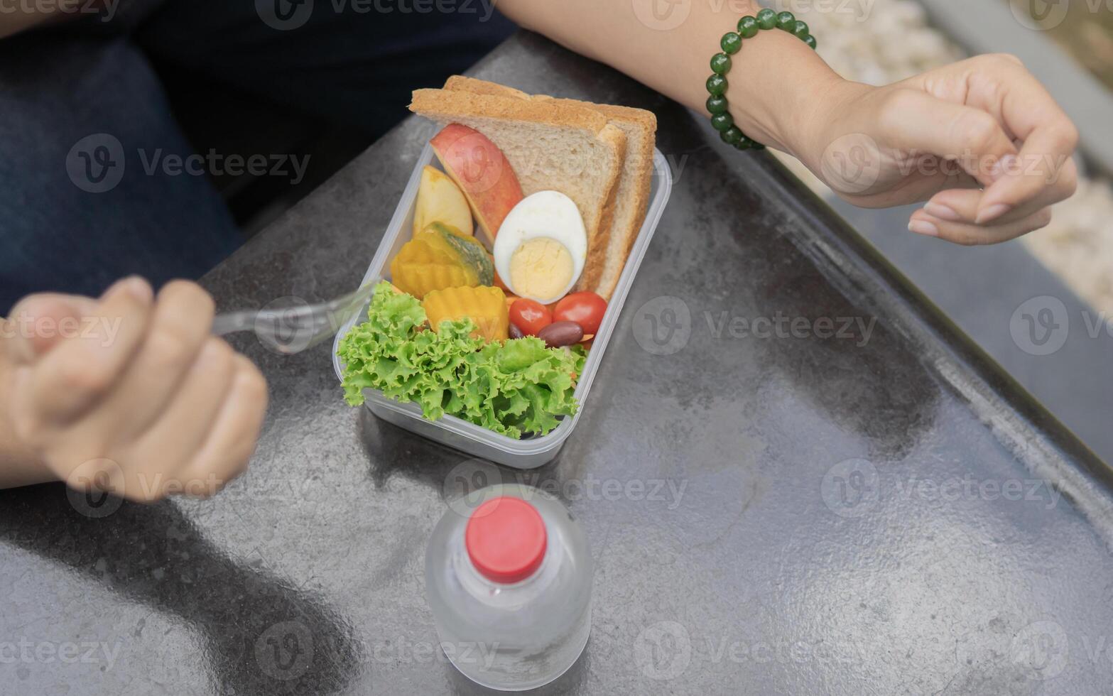 Top view of female hands eating her lunchboxes with salad and fruits at outdoor. photo