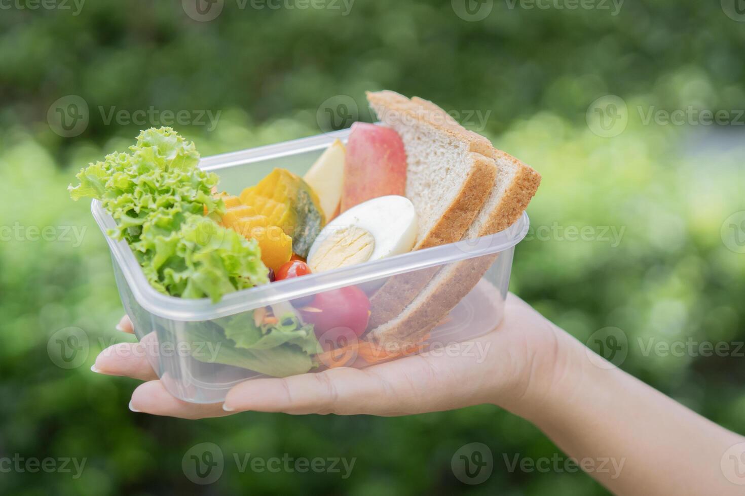 Woman enjoys a picnic in the park, she show her lunch box filled with a variety of fresh fruits and vegetable. photo