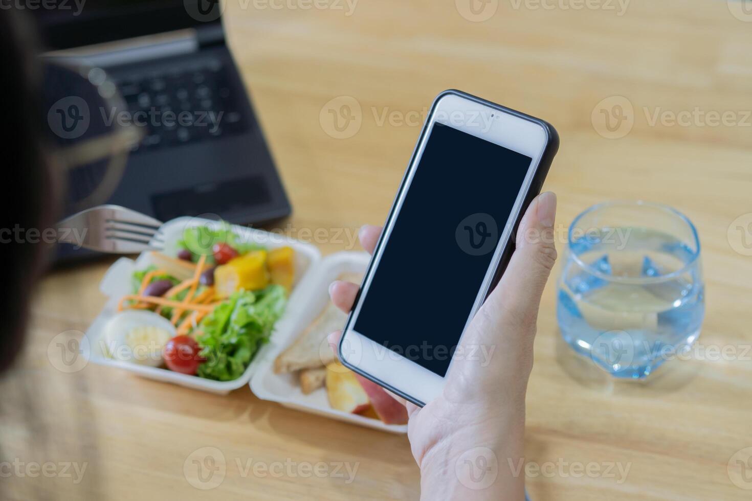 Close-up of woman eat lunch with healthy food when using smartphone. photo
