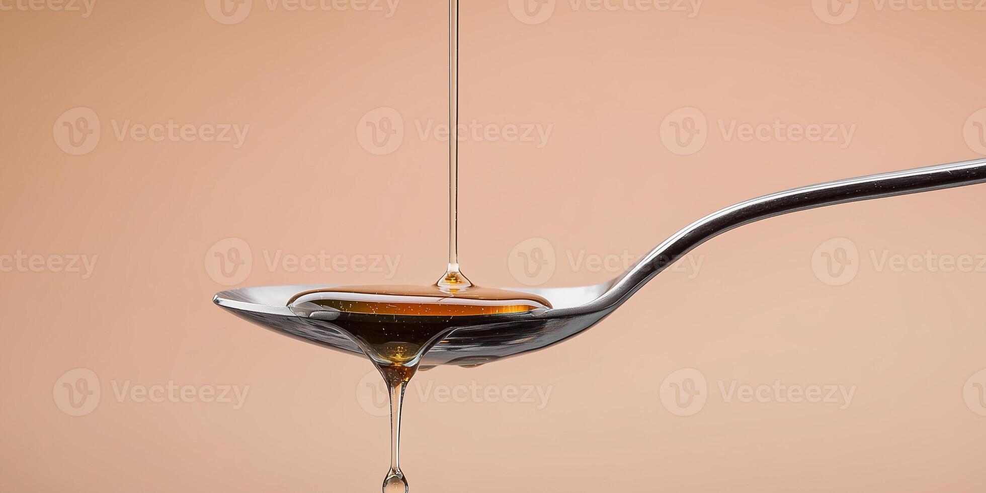 Small drop of honey frozen mid-drip above silver spoon against pale peach background photo