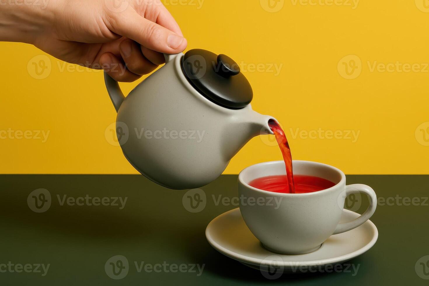 Hand pouring vibrant red tea from grey ceramic teapot into matching teacup photo