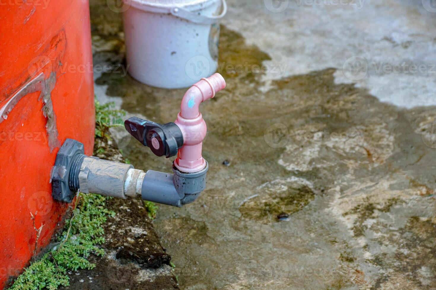 Water Tank with Faucet and Bucket on Wet Concrete Surface photo