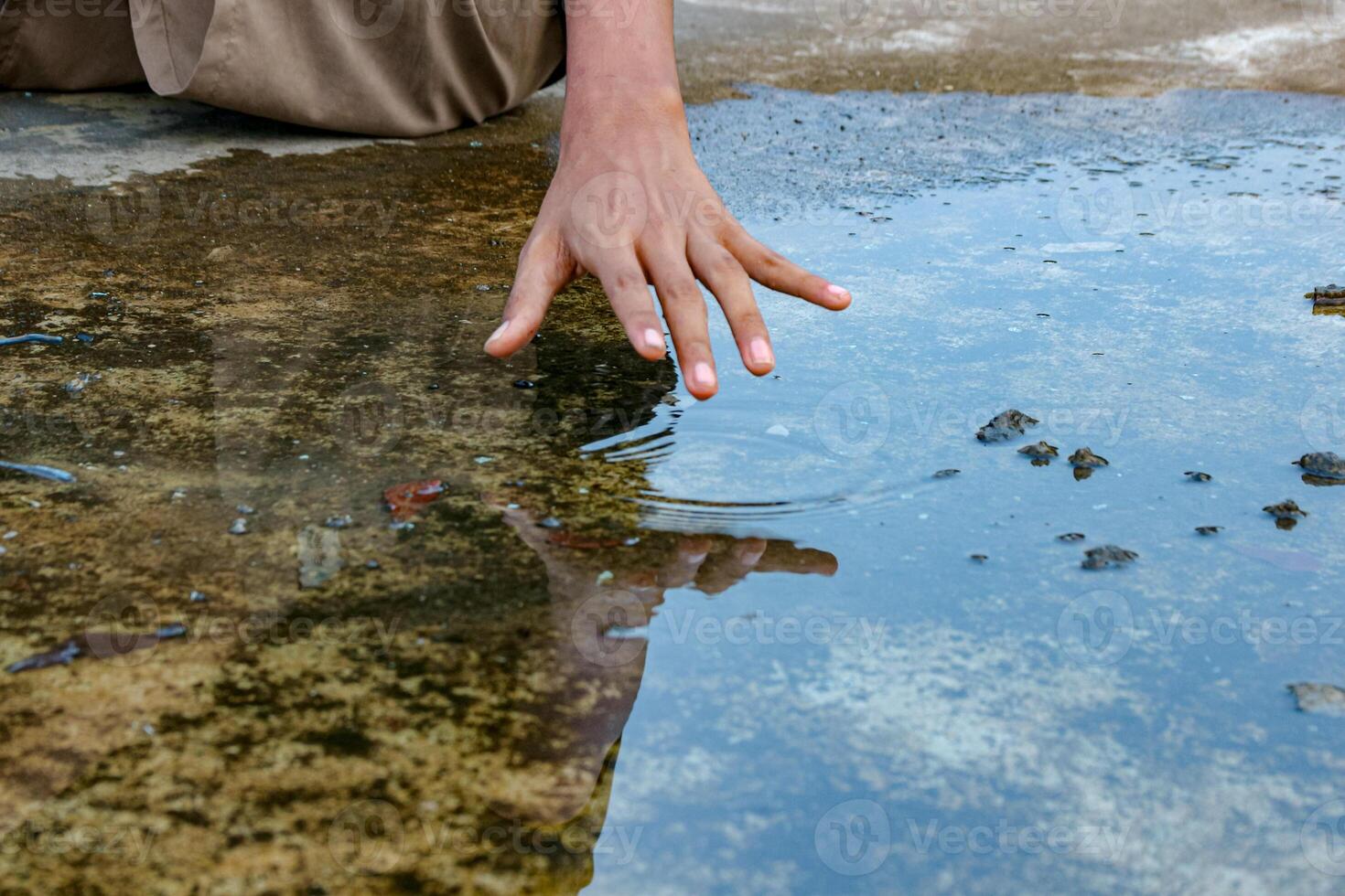 Hand Touching Water Surface in a Puddle Creating Ripples photo
