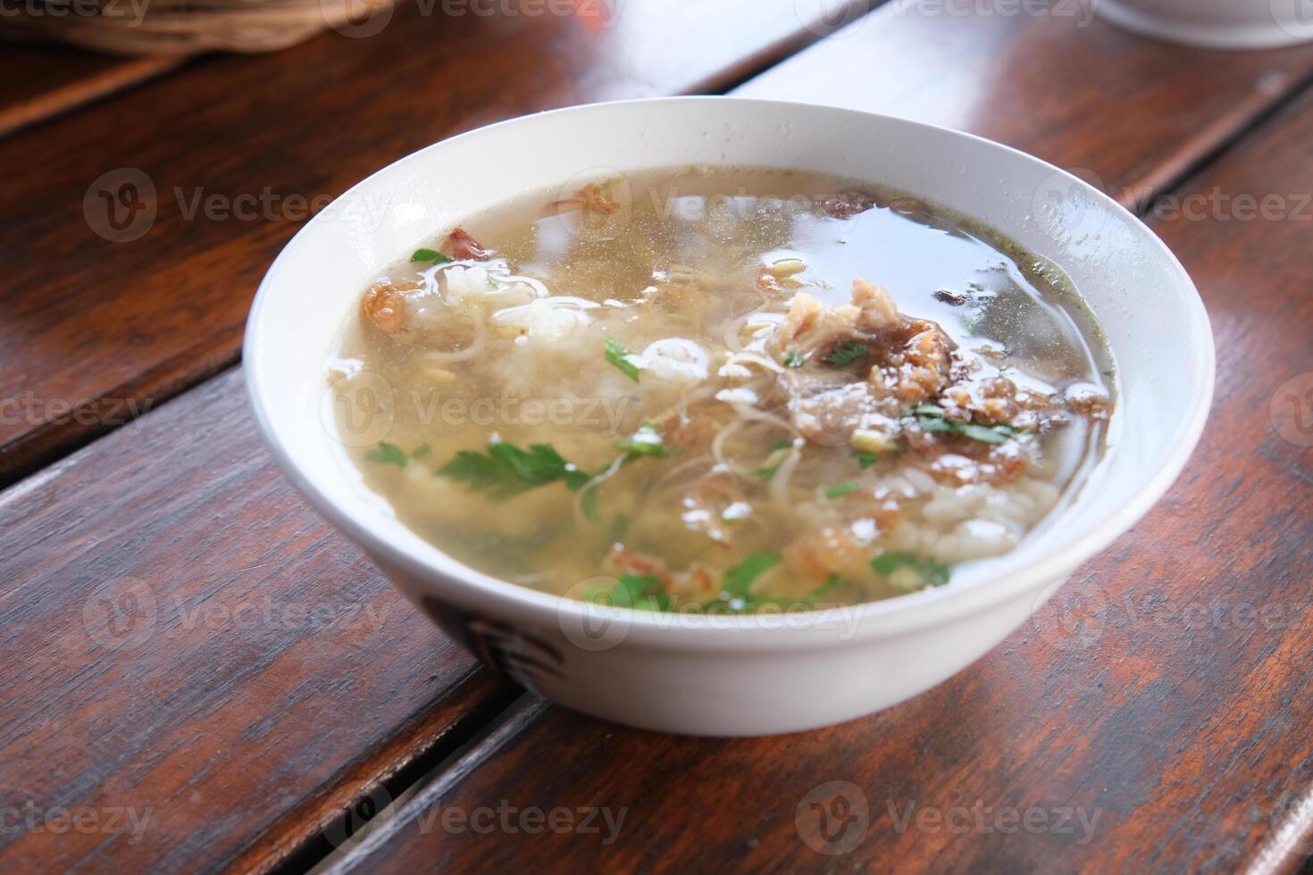 Serving of Indonesian Soto Ayam Soup on Wooden Table Close Up photo