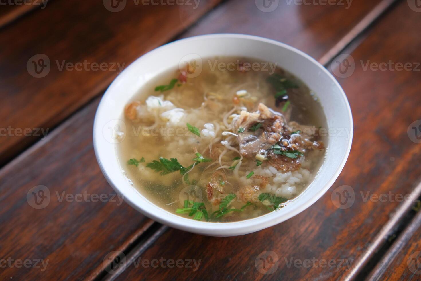 Bowl of Soto Ayam Chicken Noodle Soup on Wooden Table Surface photo