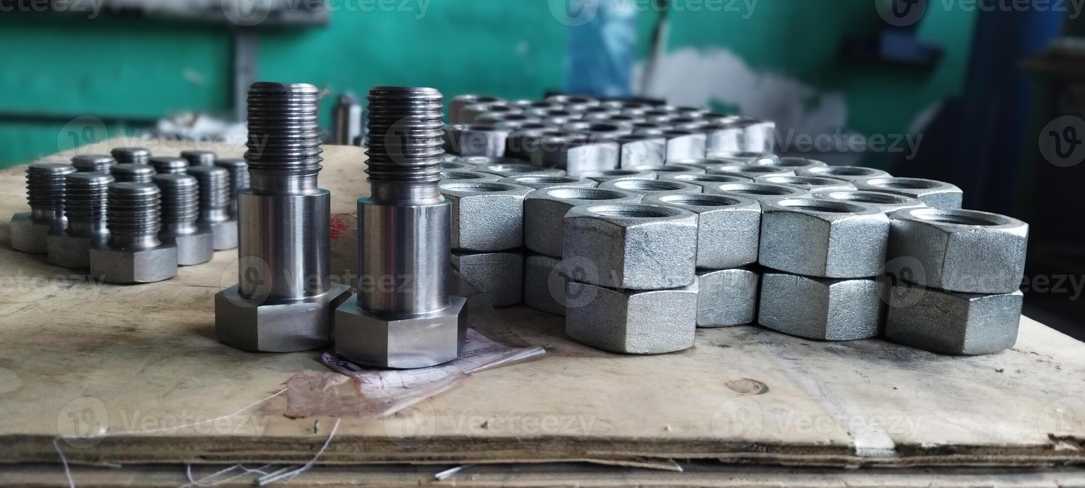 Close-up of new metal bolts and nuts. Steel bolts and nuts. Industrial fasteners displayed on a wooden surface, with a blurred workshop background. Flanged steel hex nuts. Mechanical engineering. photo