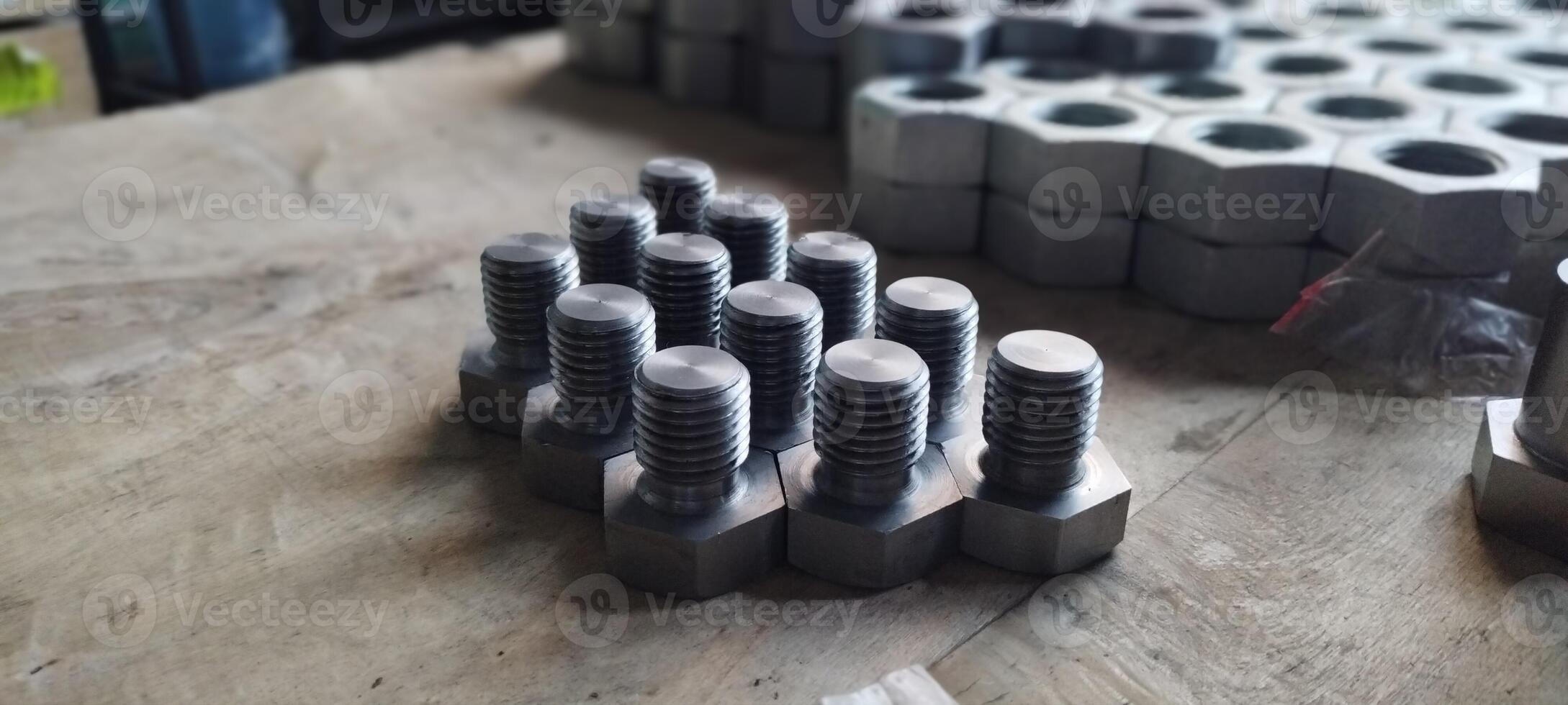 Close-up of a set of new metal bolts. Hex head bolts in focus, with nuts in the background. Industrial fasteners on a wooden surface. Selective focus with blurred background. photo