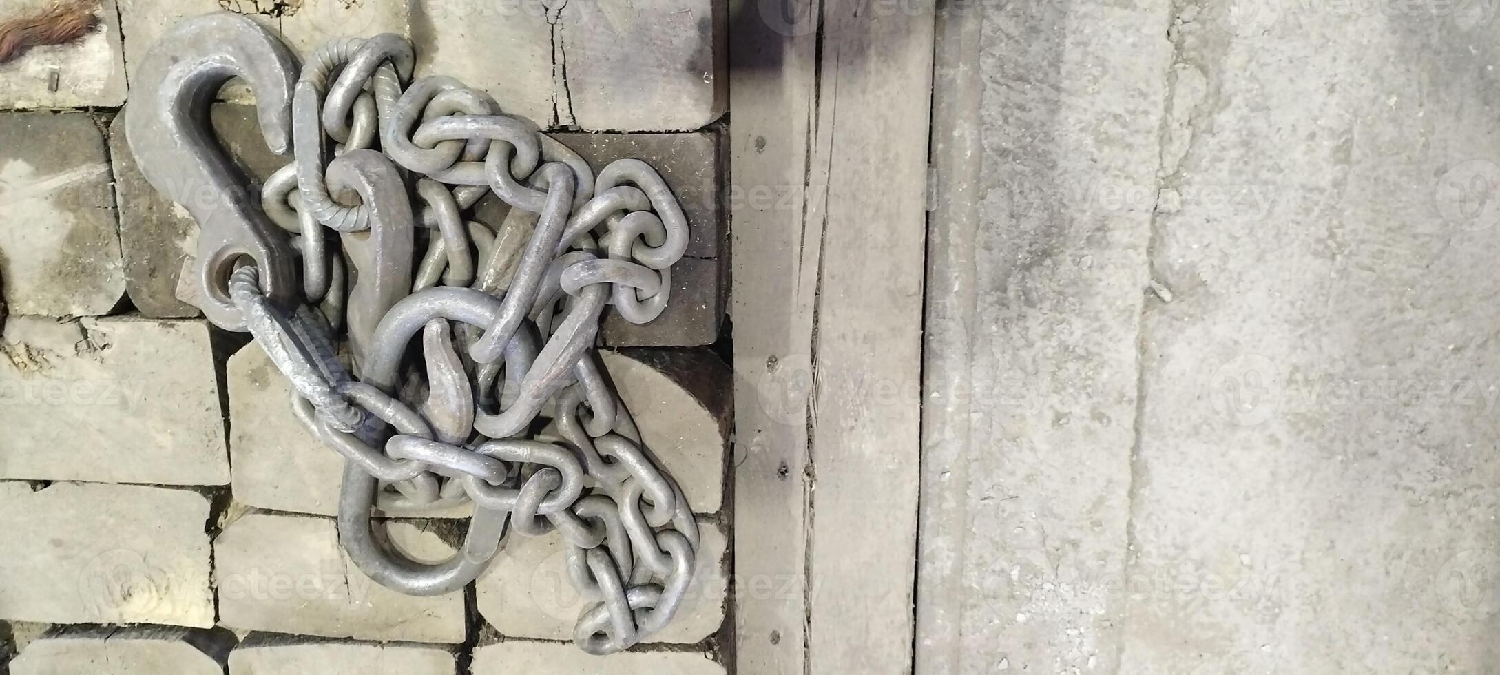 Heavy duty metal chain and hook on a brick and concrete surface. Industrial lifting equipment with a rustic, worn texture. Metal chain link hook background. Grunge style industrial background. photo