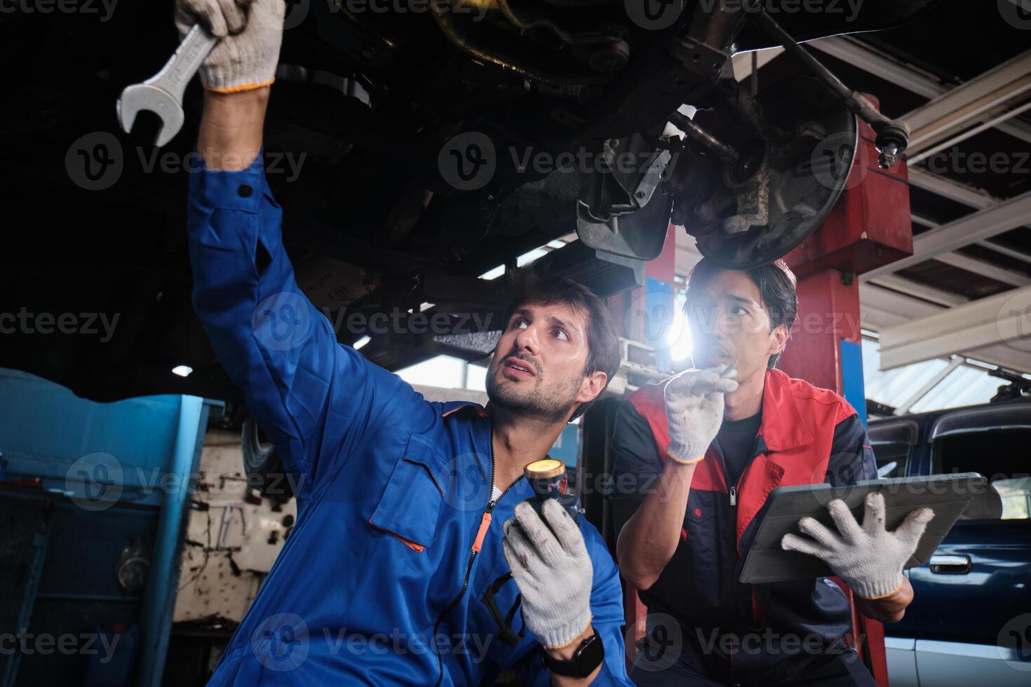 Two male mechanics cooperate, Latin and Asian workers fixing automotive wheels and maintaining car suspensions in garage, and technician engineering service works in vehicle transport industry. photo