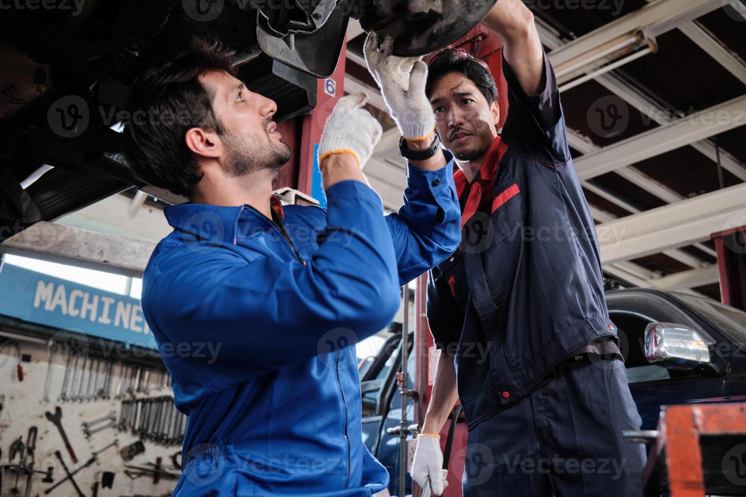 Two male mechanics, Hispanic and Asian workers fixing automotive wheels and maintaining car suspensions in garage station, and technician engineering service jobs in vehicle transport industry. photo
