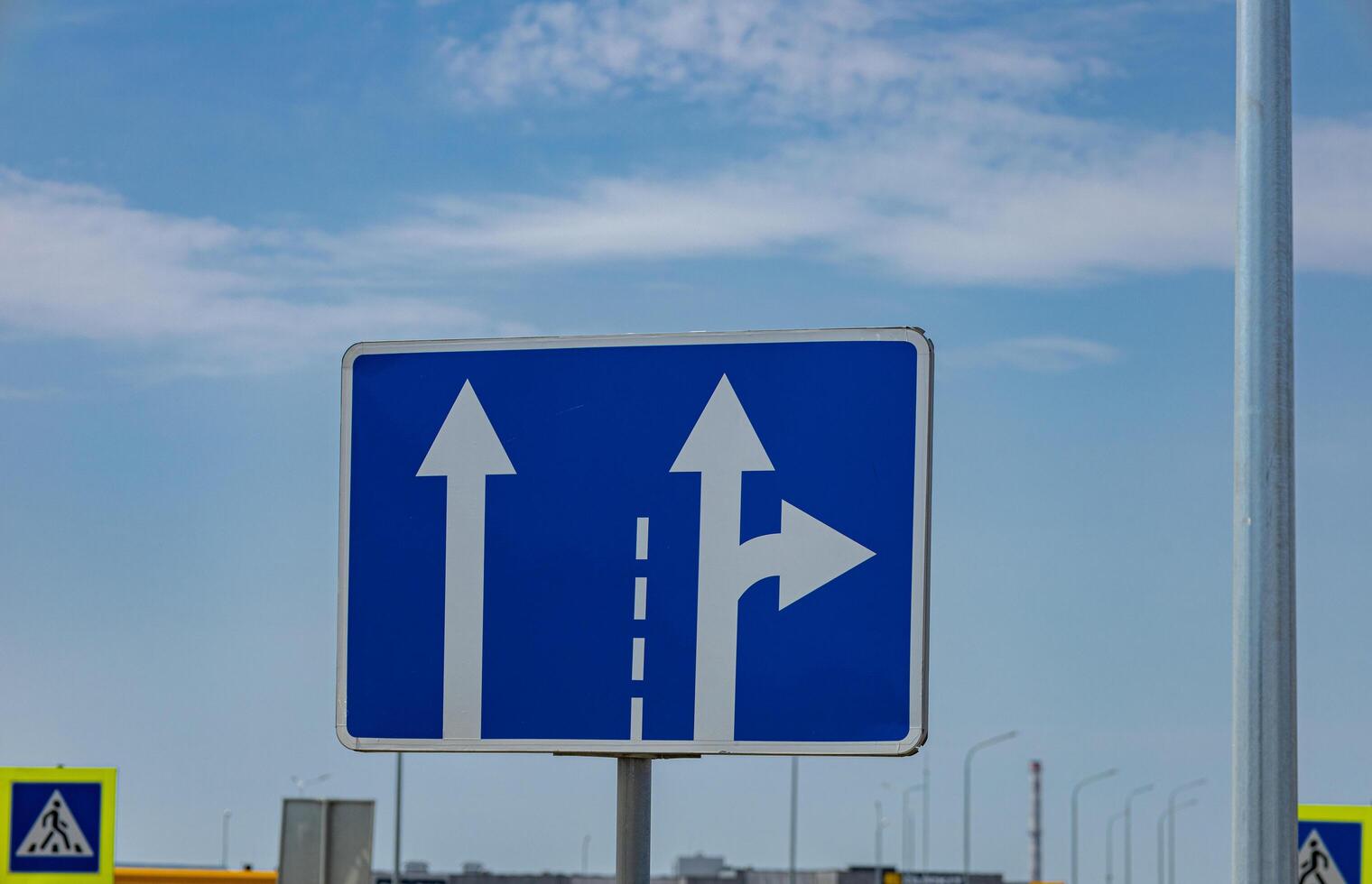Traffic sign displays arrows showing the option to continue straight or turn right at an intersection in sunny weather photo