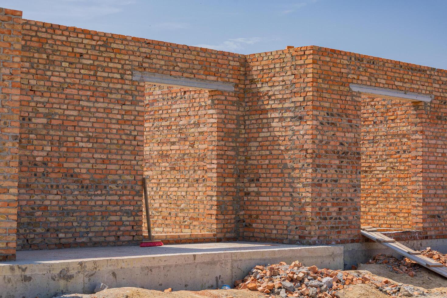 Brick walls are being constructed as part of a new building project under clear skies and bright sunlight, showcasing progress in the area photo