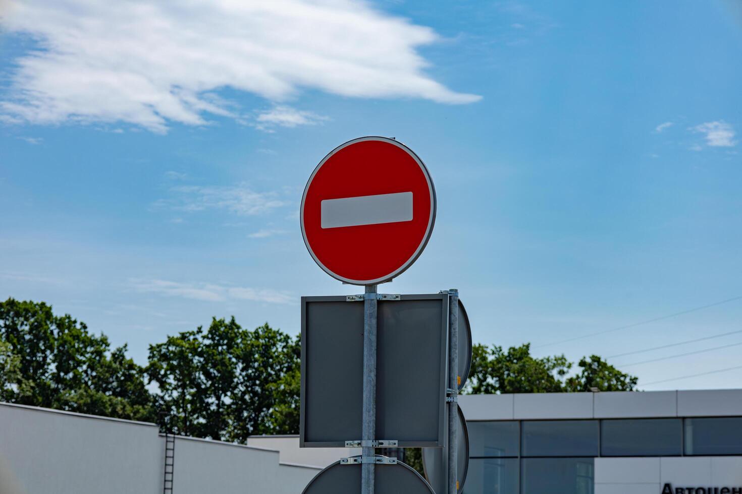 A circular no entry sign stands prominently against a blue sky, indicating restricted access to vehicles near a contemporary structure photo