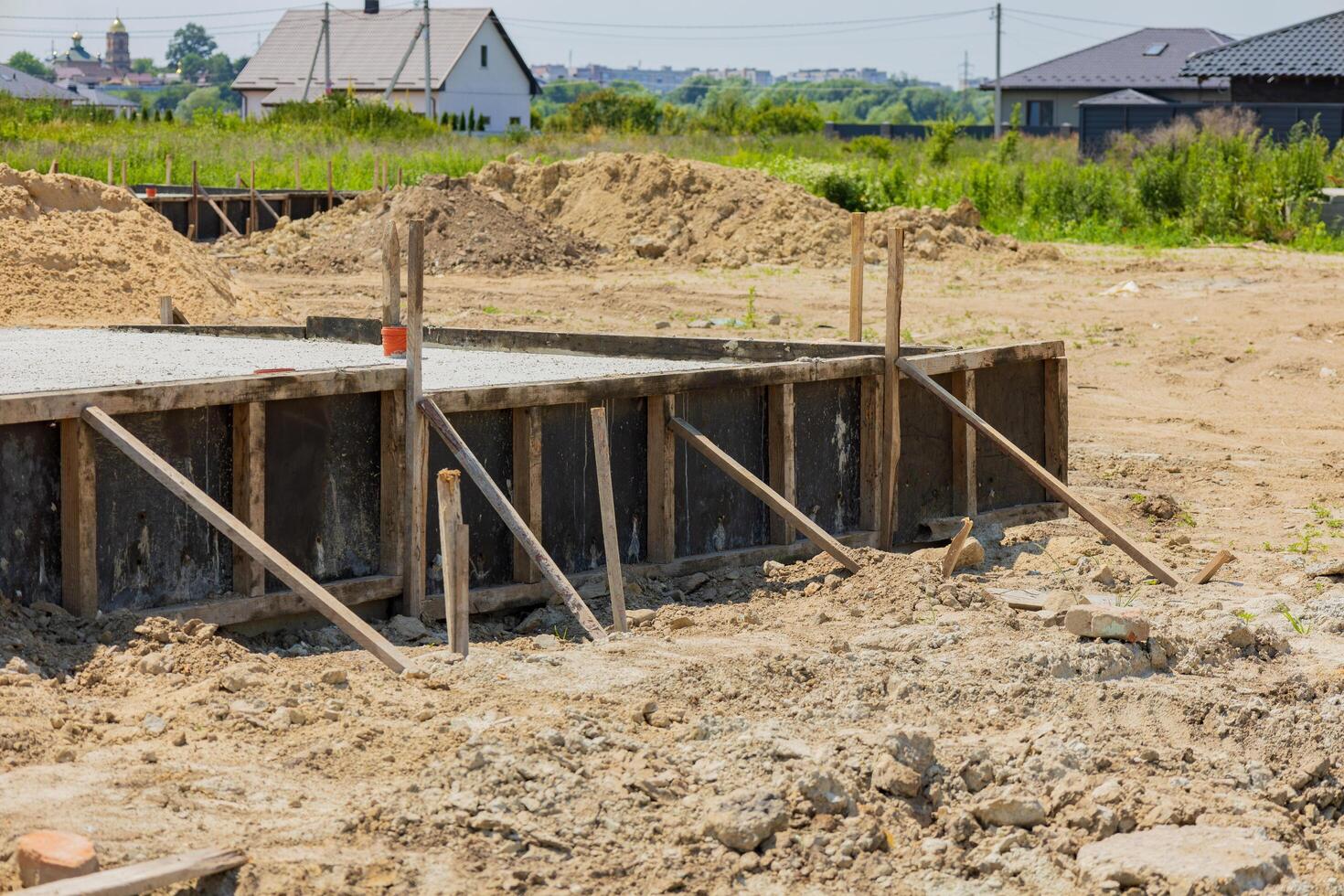Workers are setting up a foundation with wooden supports at a construction site surrounded by greenery and houses photo
