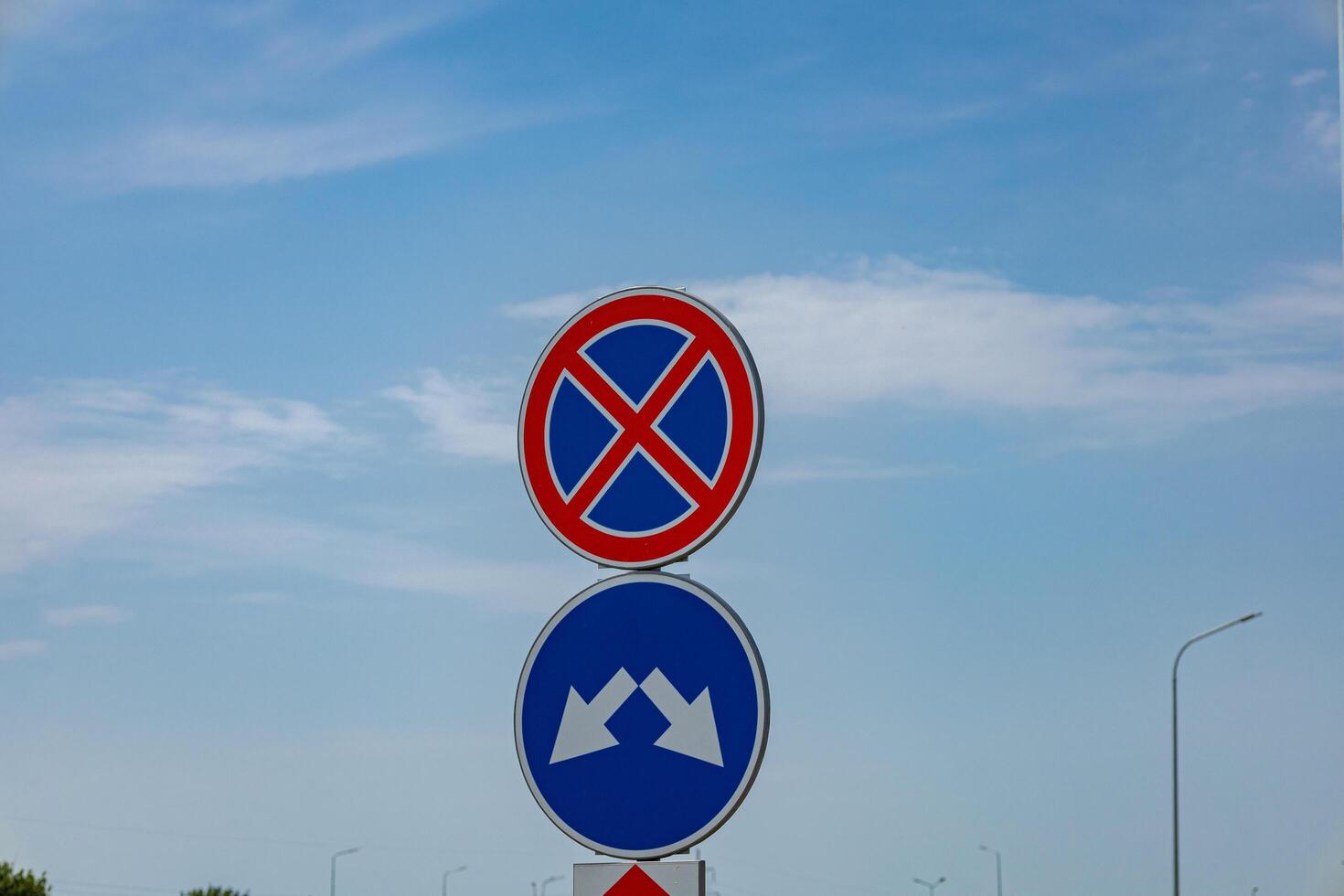 Road signs indicate no parking regulations and a yield instruction against a clear blue sky in an urban environment photo