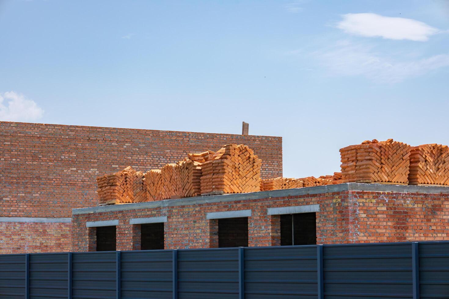 Bricks are neatly stacked on a building structure at a construction site, surrounded by a blue sky. The setting reflects a sunny summer day photo