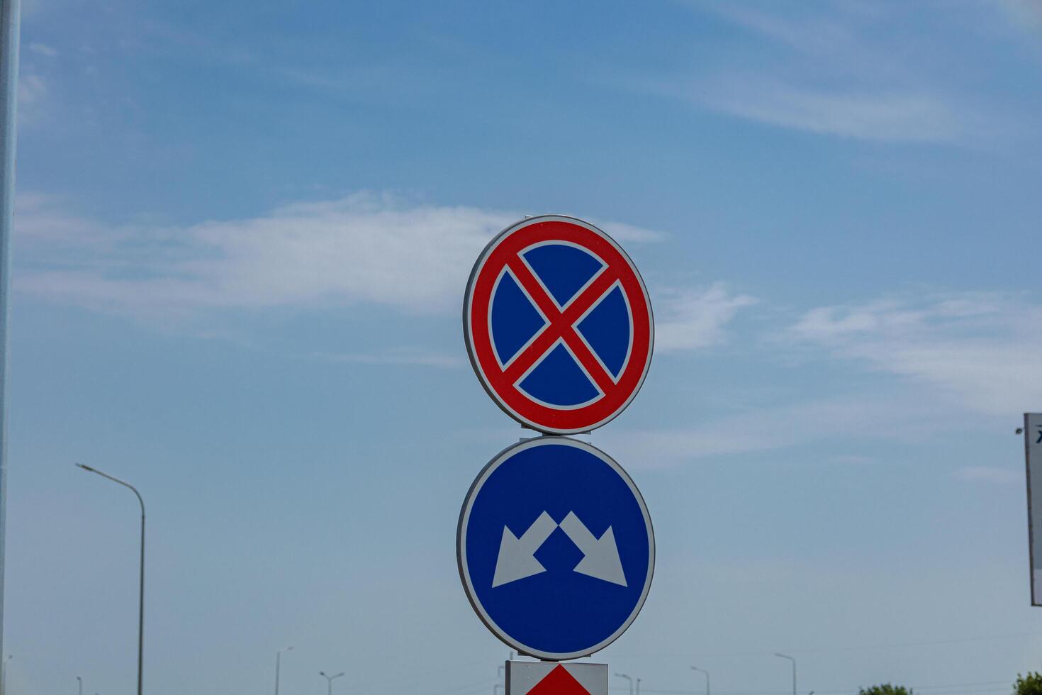 Two road signs indicating no parking and a specific direction are prominently placed against a bright blue sky, highlighting traffic regulations photo