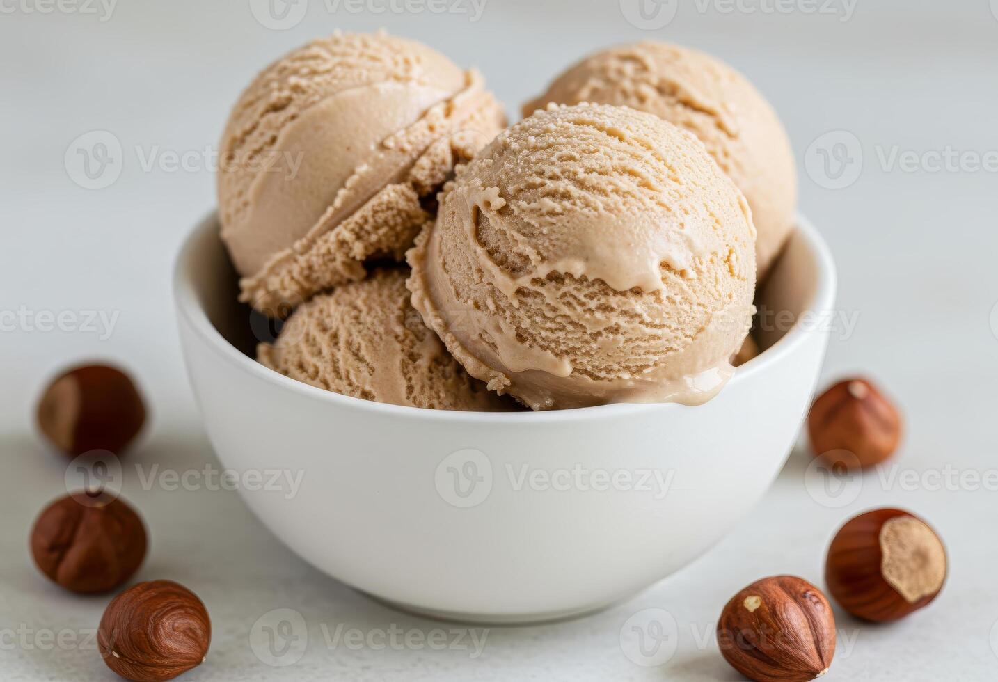Close-up of a white bowl filled with three scoops of hazelnut creamy ice cream, garnished with a hazelnuts photo