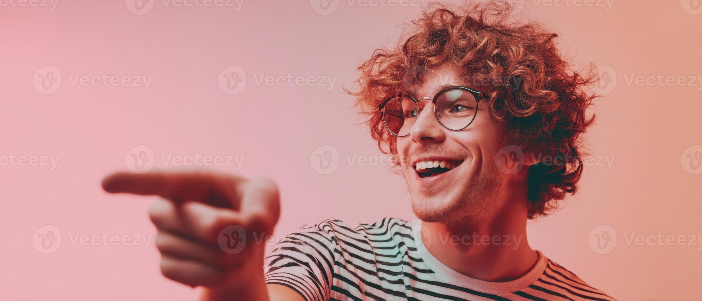 The cheerful young man with curly hair pointing and smiling joyfully. photo