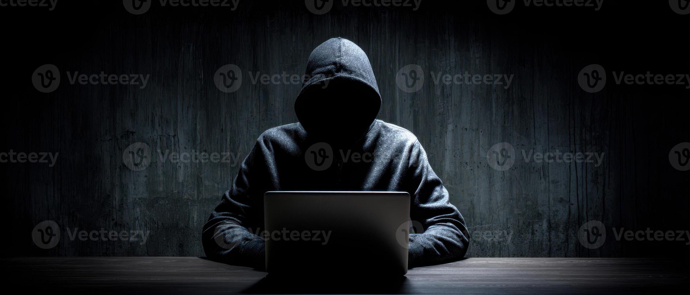The mysterious hacker working intently on a laptop in a dimly lit environment. photo