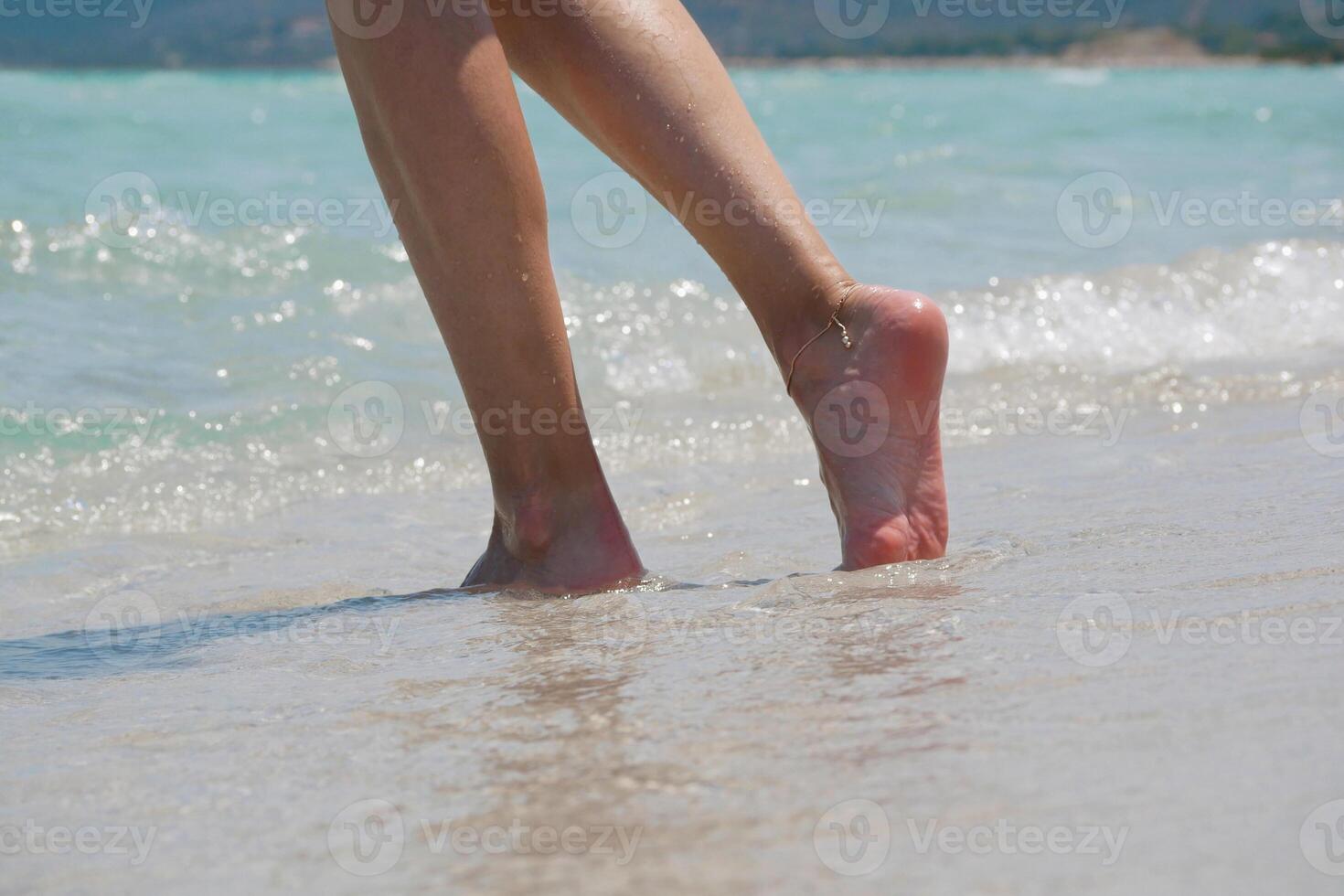 Close-up of female legs walking barefoot along the beach with sea waves. Wellness, travel and lifestyle concept. photo
