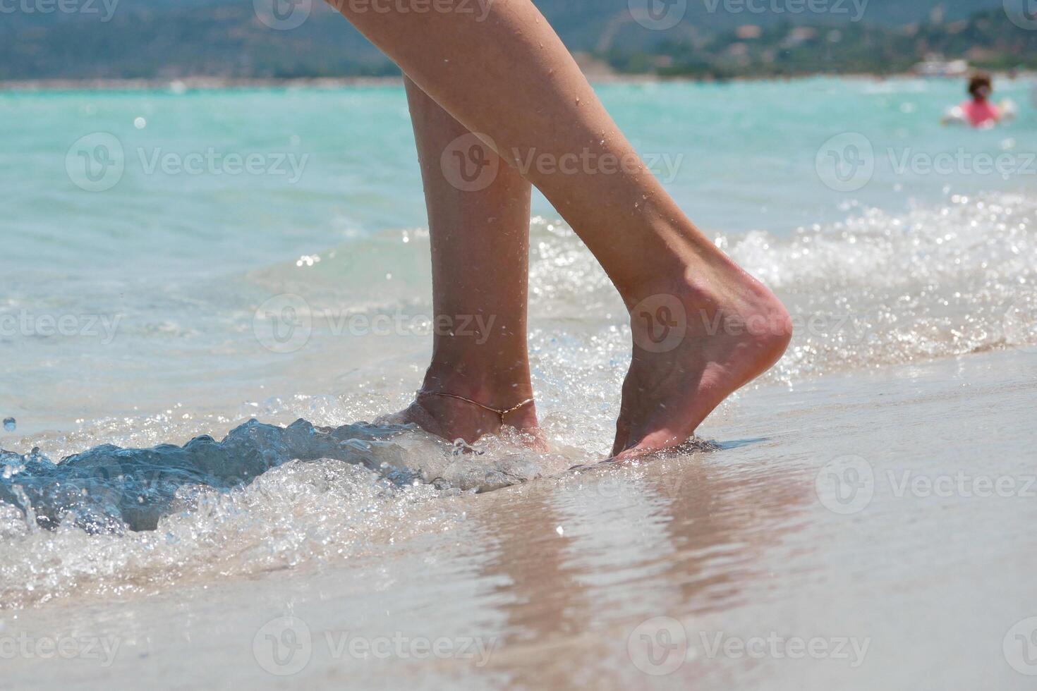 Close up of female legs walking barefoot along the beach with sea waves. Wellness, travel and lifestyle concept photo