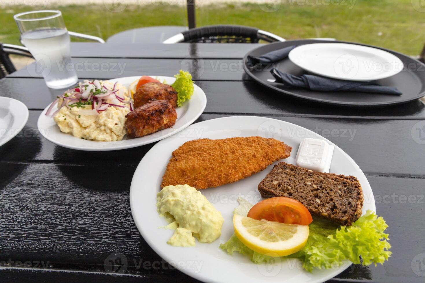 restaurant on the seashore. White plate with fish patties, fish fillets and potato salad. photo