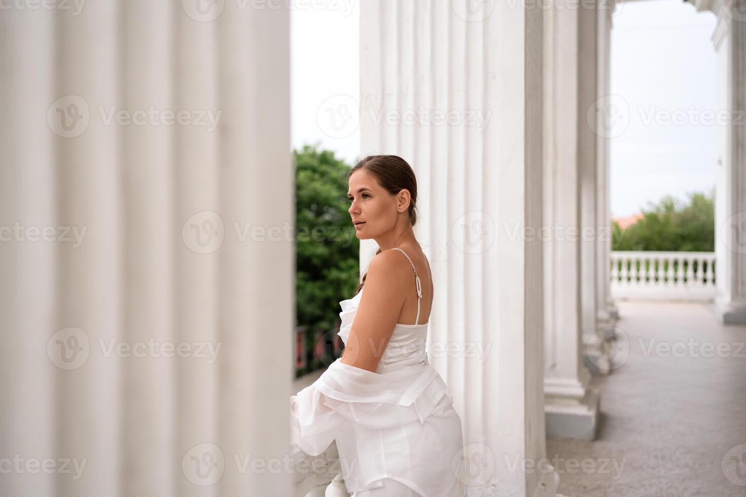 Woman Columns Balcony. Lady in white looks outward from a columned balcony during daytime. photo