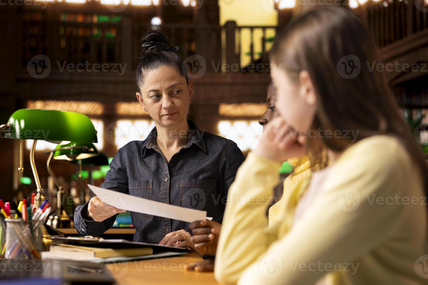Woman teacher helping students prepare for an exam by providing materials for learning, fostering concentration and guiding them through their school curriculum. Mentor ensures success. photo