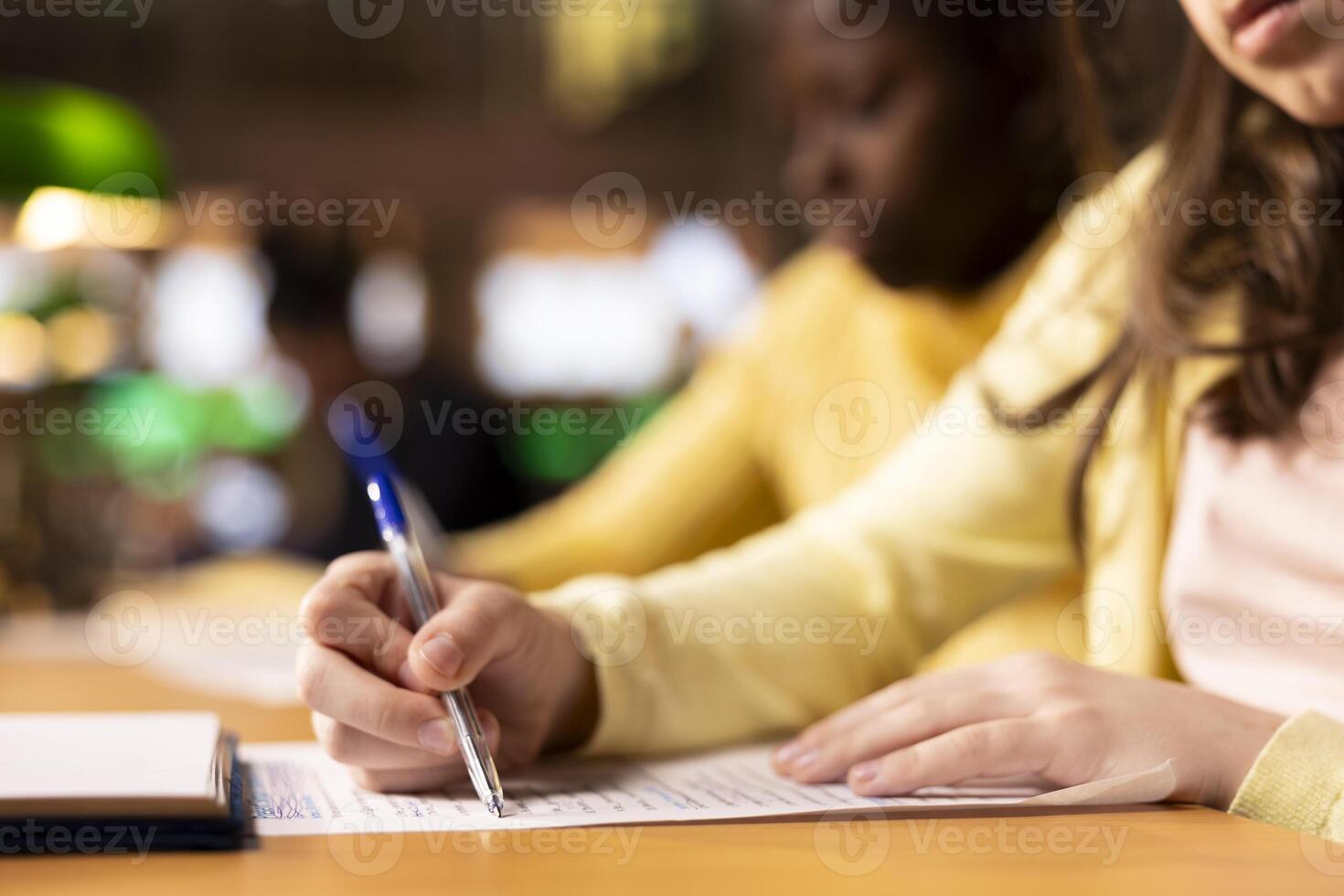 Multiethnic teens finishing their homework at a library after classes, engrossed in literature and notes. Pupils writing an essay for the school assignment, productive study sessions. Close up. photo