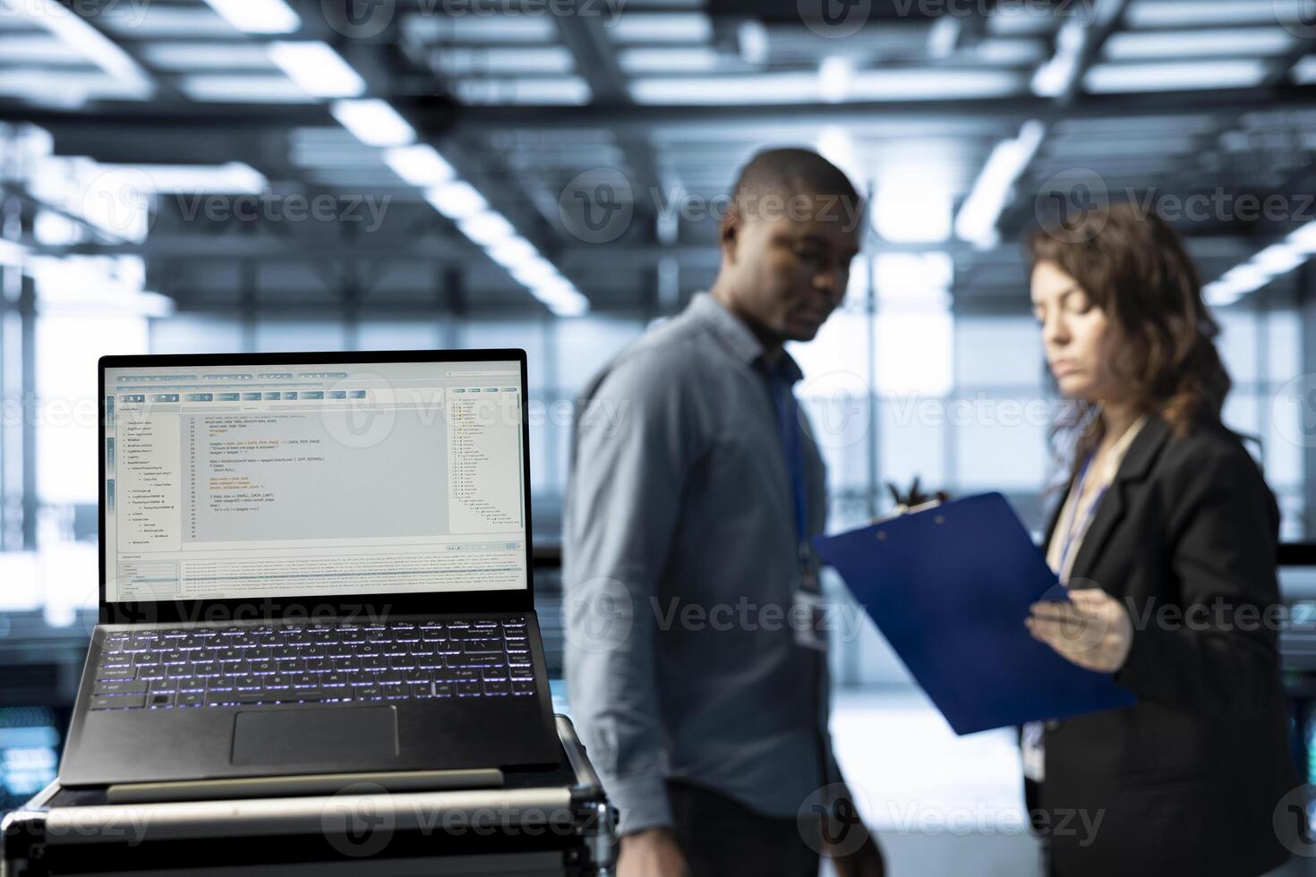 Lines of code on laptop screen in data center with programmers in blurry background. Close up of programming language on notebook display used by IT experts inspecting server clusters photo