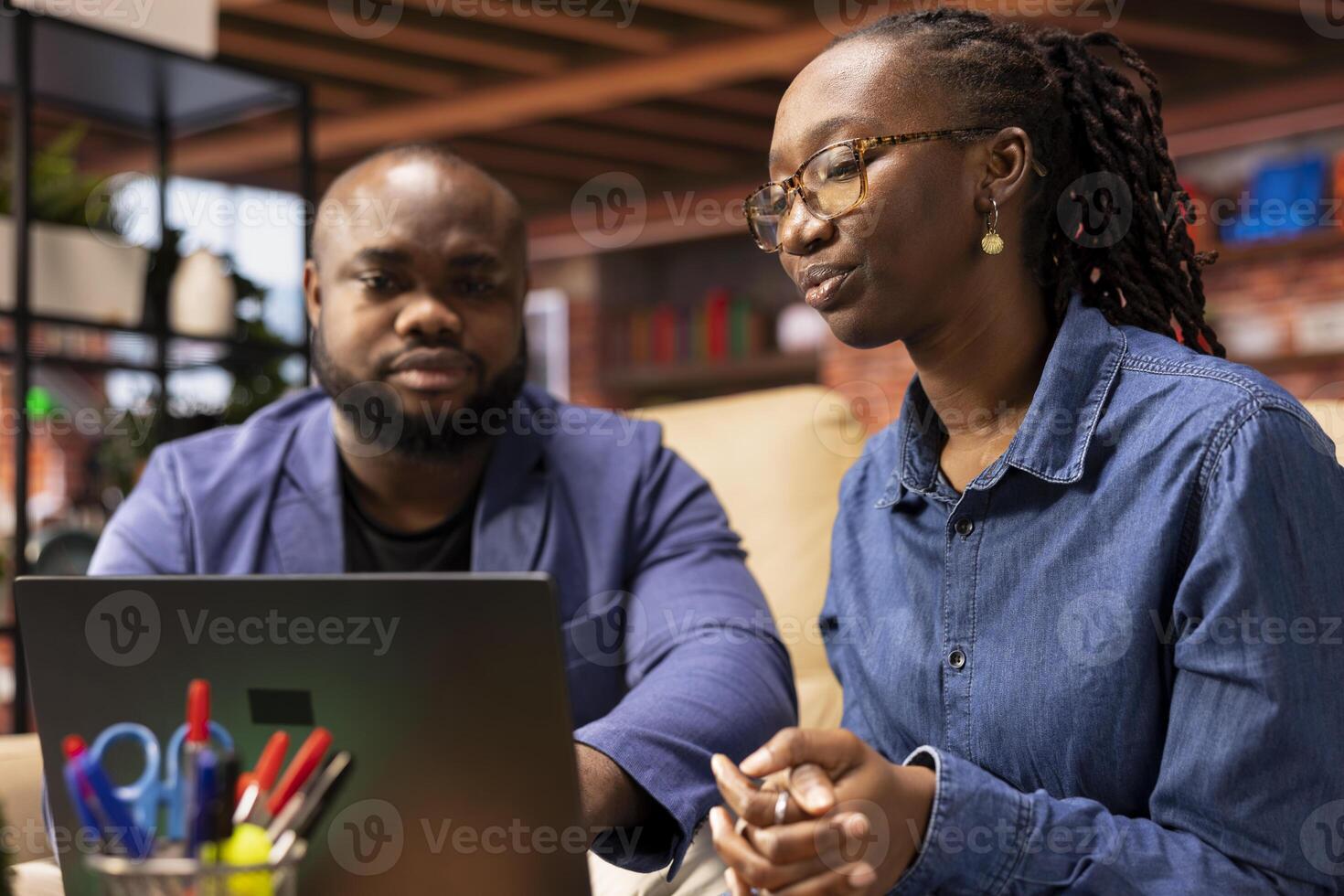 African american couple sitting on couch to share a business idea, using modern technology and tools to analyze trends and boost success. Freelancers improving workflow efficiently. photo