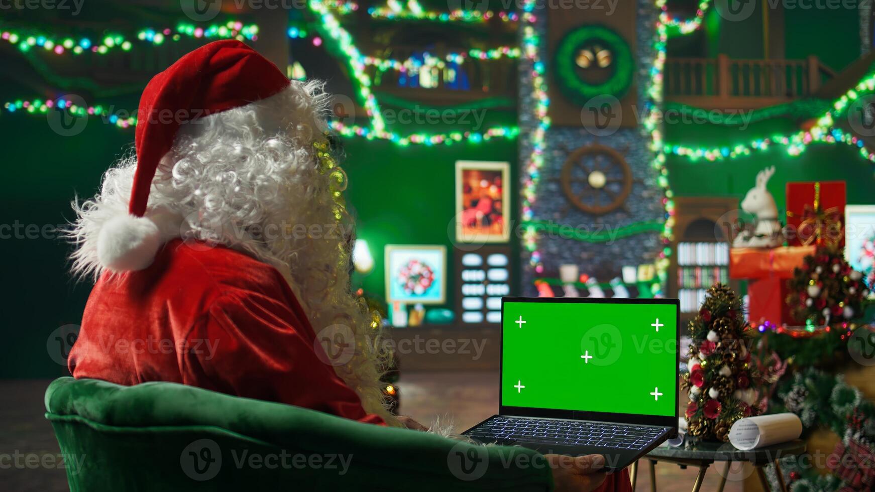 Santa Claus performer typing on green screen laptop, preparing shipping parcel with gift to be sent to kids. Man uses mockup notebook, scheduling goods delivery, preparing to send presents to children photo
