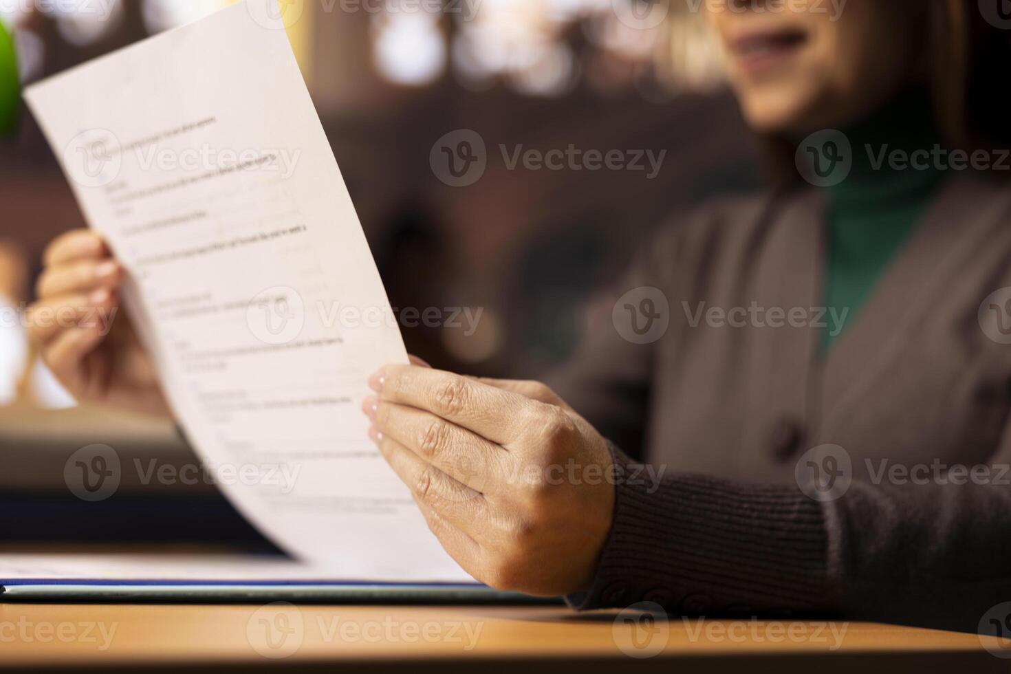 Mature student reviews paperwork for her degree in a classic library setting, using multiple academic sources and books. showing determination to complete her master degree thesis. Close up. photo
