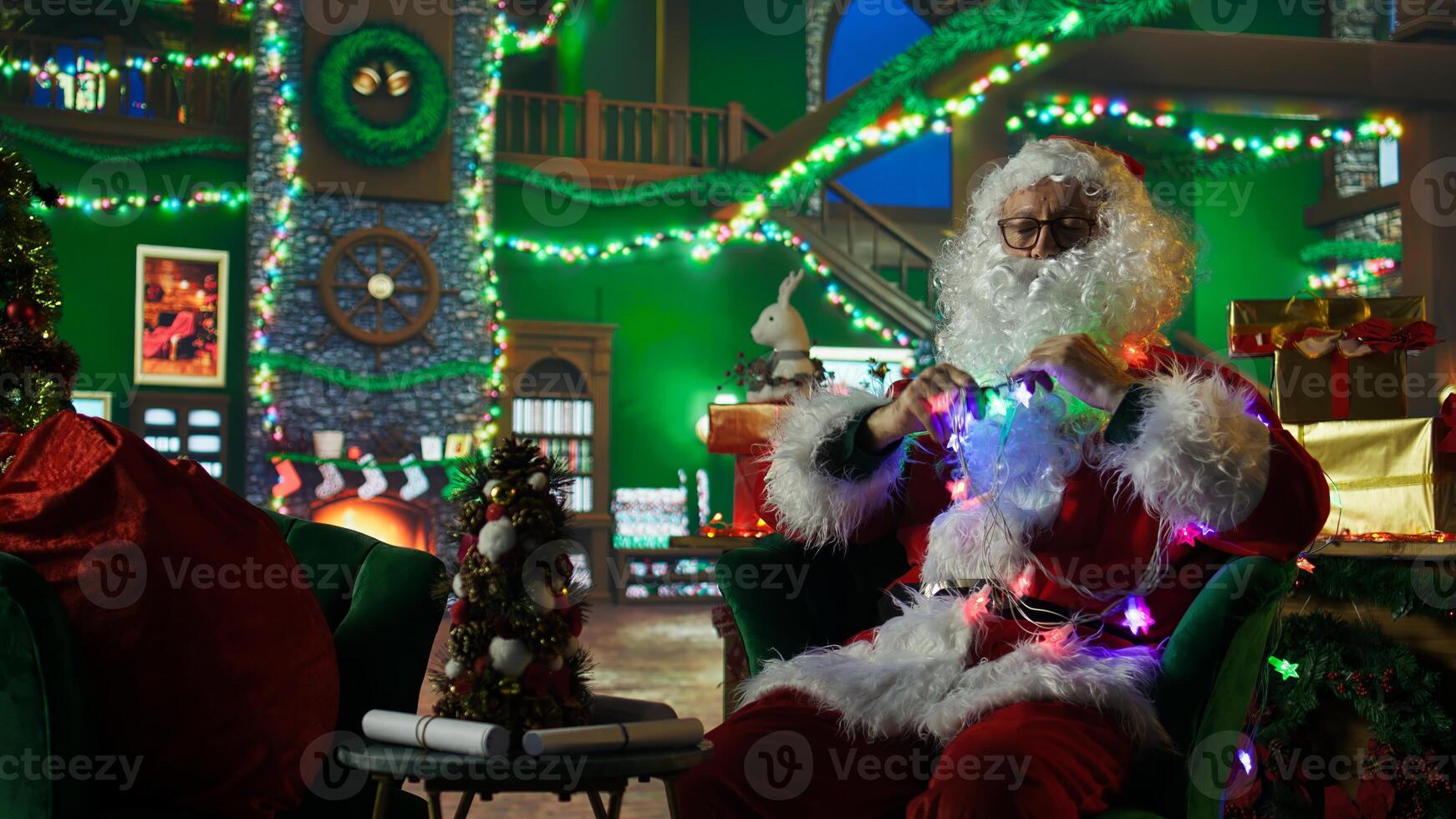 Santa Claus entangled in led lights while adorning workshop for Christmas, preparing it for families visiting. Costumed man knotted in xmas lights while doing holiday season decorations, camera A photo