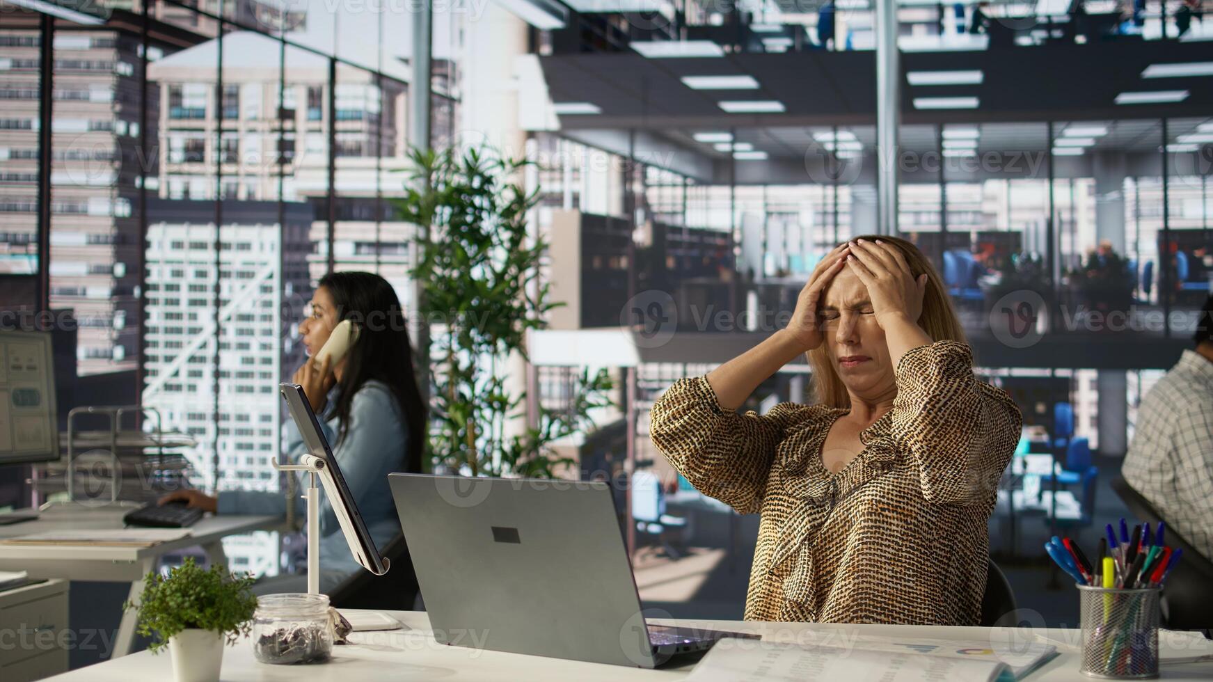 Sleepy overworked female employee yawning at her office desk, feeling exhausted with her work and suffers burnout. Businesswoman dealing with fatigue and low energy, challenges at job. Camera B. photo