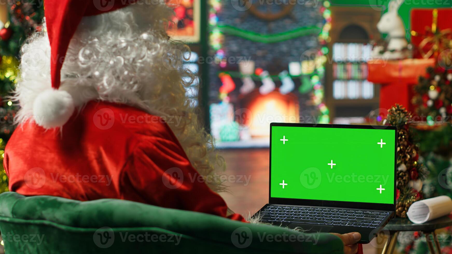 Santa Claus making list of kids who has been naughty or nice on green screen laptop. Person preparing travel plans on chroma key notebook before visiting children, camera A photo