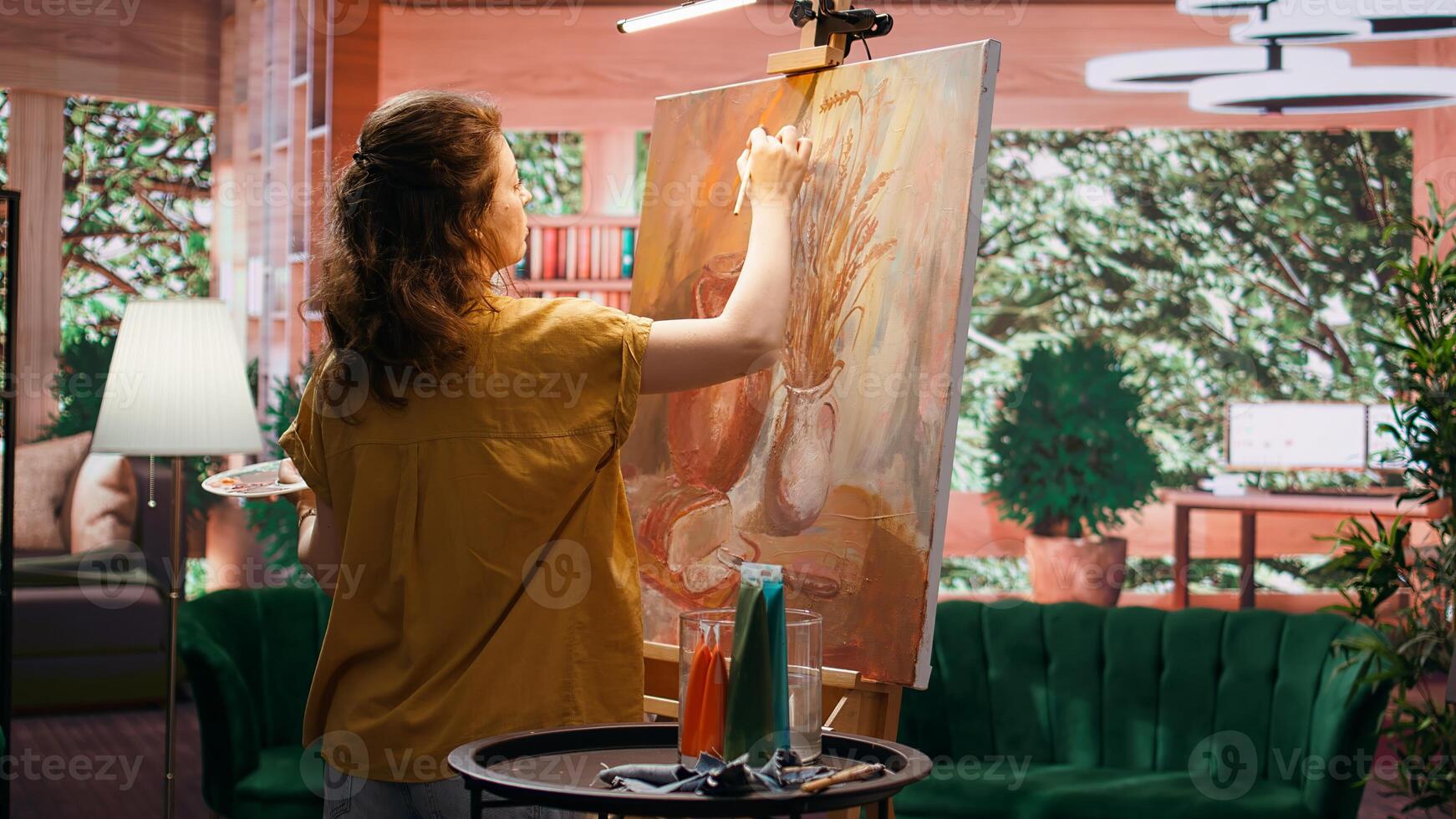 In a rustic workshop, artist mixes a variety of watercolor paint on palette to create a colorful masterpiece on canvas. Woman painting with a brush and showing her skill, artwork creation. Camera B. photo