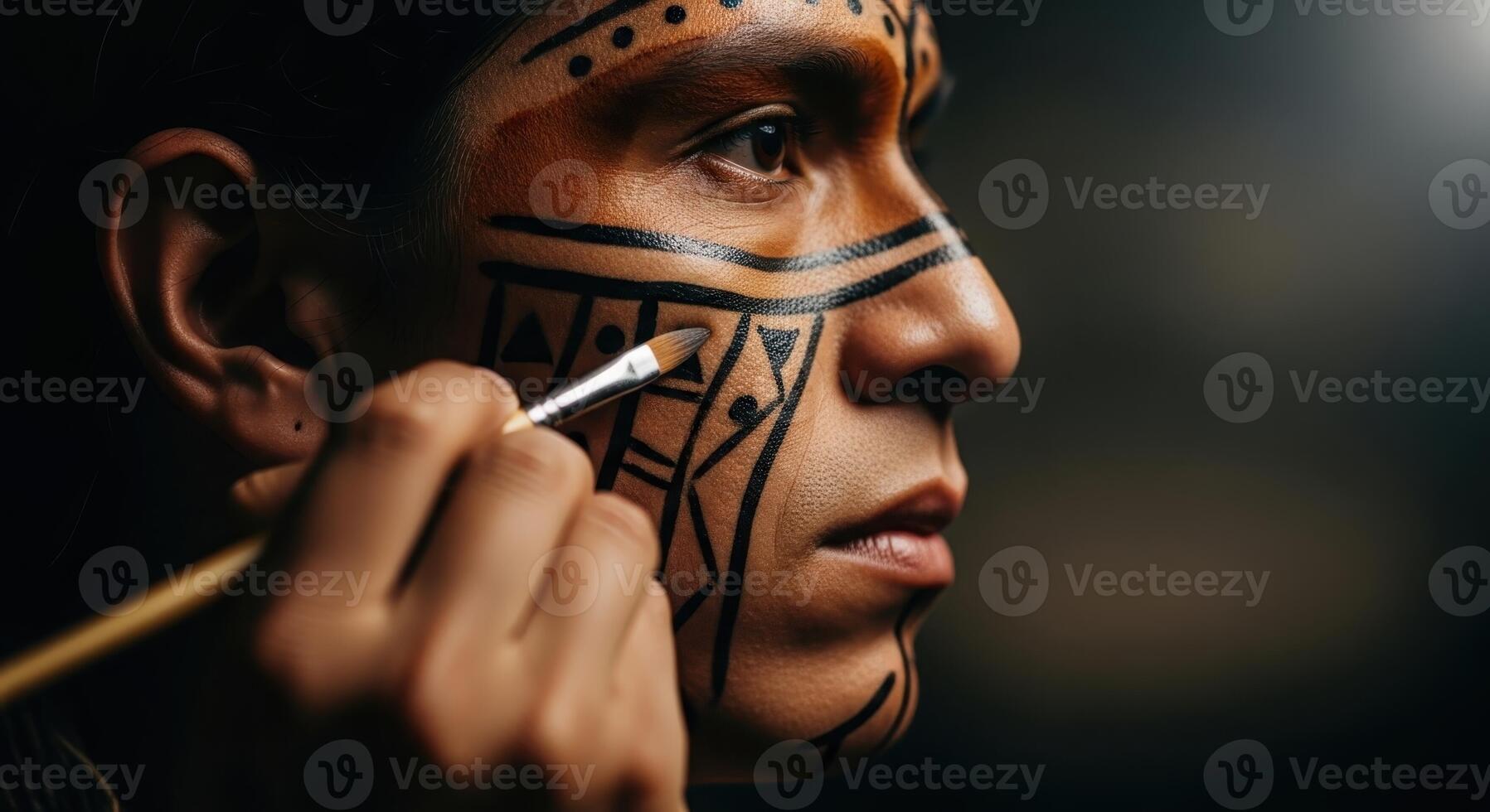 Close up profile of a man applying intricate tribal face paint with a brush photo