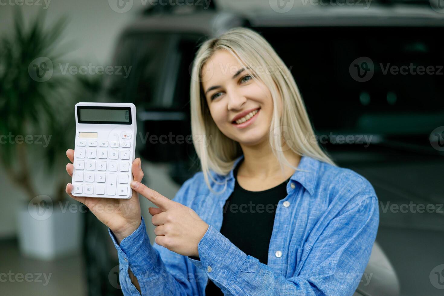 Saleswoman showing calculator and explaining car cost in dealership photo