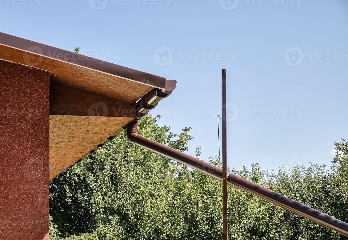 Modern house roof detail with a drainpipe against a clear blue sky. Rain water harvesting architecture. photo