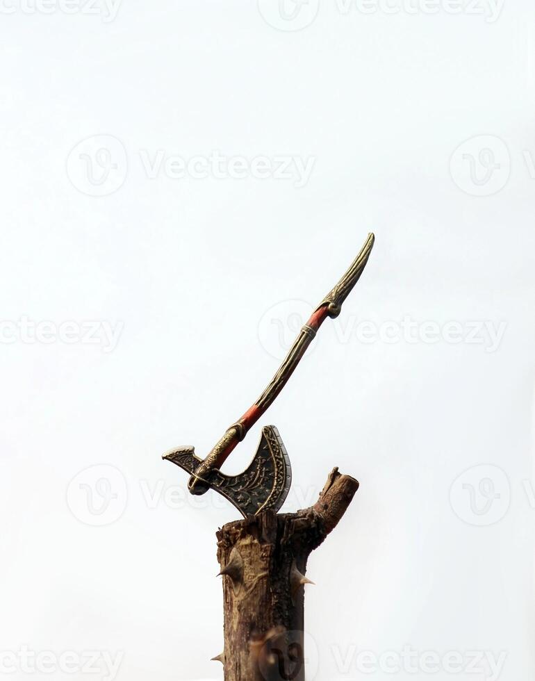 Tiny ancient ax firmly planted in a wooden stump. Ax blade is made of dark metal, with curved handle. Texture of wood and metal is clearly visible. photo