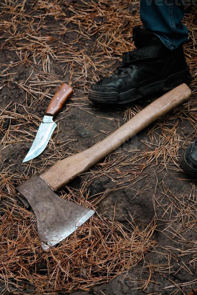 An Axe And A Knife Lie On Pine Needles Next To A Person's Boot. photo